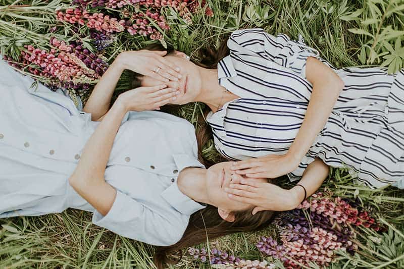 Two people laying side by side covering each others eyes.