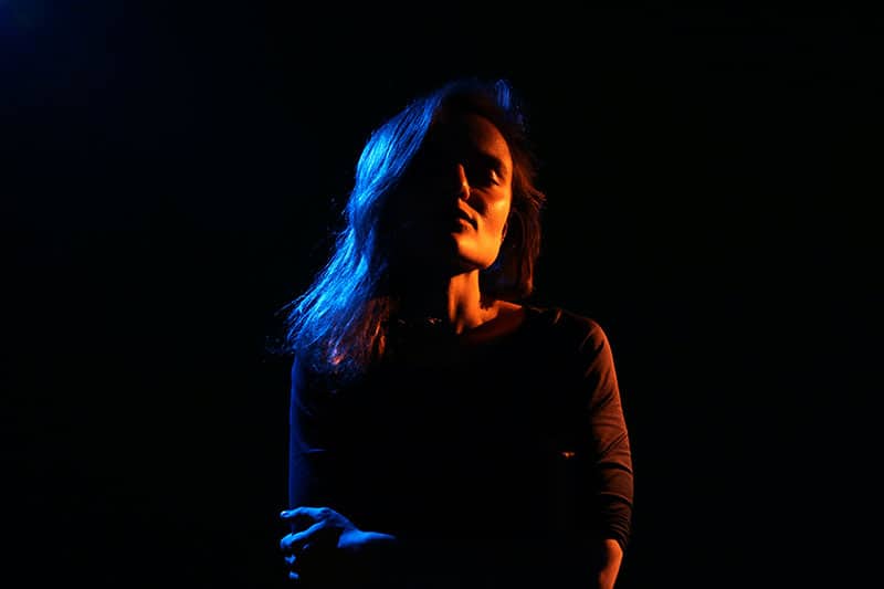 A darkly lit woman with her arms folded